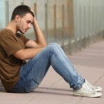 Teenager boy worried sitting on the floor with a hand on the head